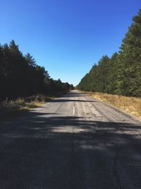 Road amidst trees against clear blue sky