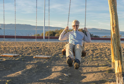 Portrait of smiling woman sitting on swing at beach