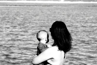Side view of woman carrying baby while standing against sea
