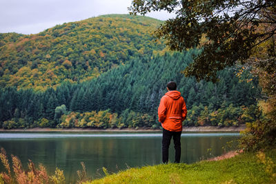 Rear view of man standing by lake against trees