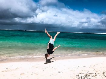 Full length of young man jumping upside down at beach against sky during sunny day