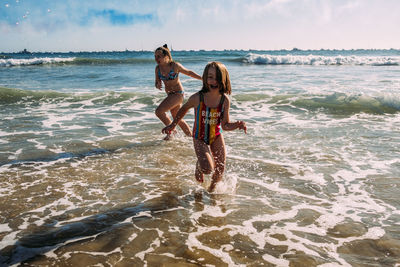 Siblings running in water at beach on a sunny day