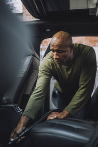 Bald mature man cleaning car with vacuum cleaner