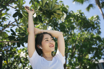 Young woman looking away while standing against tree