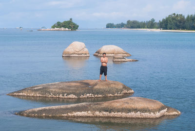 Shirtless man standing on rock amidst river