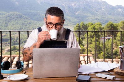 Mid adult man holding coffee while sitting on table