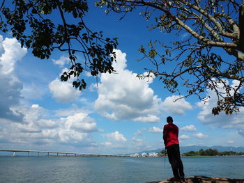 Rear view of man standing by tree against sky