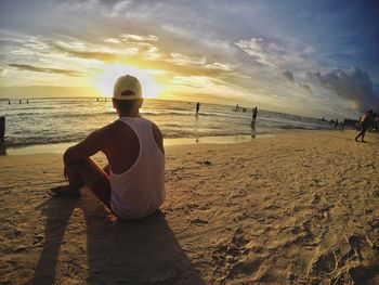 Rear view of man on beach against sky during sunset