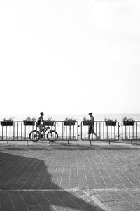 People riding bicycle on street by sea against clear sky