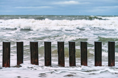 High wooden breakwaters in splashing sea waves, beautiful cloudy sky. long groynes in stormy sea