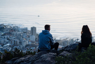 Rear view of men sitting on rock looking at cityscape