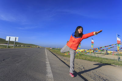 Woman doing yoga by prayer flags on road against blue sky