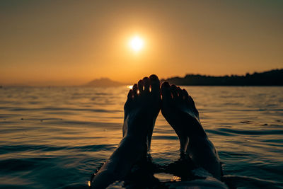 Low section of woman in sea against sky during sunset