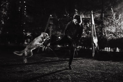 Young woman playing with dog in park at night