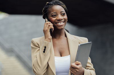 Contemplative happy businesswoman talking on mobile phone holding laptop