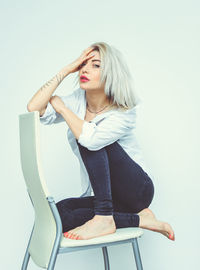 Young woman sitting on chair against white background