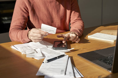 Hands of man with financial bills calculating on smart phone at desk