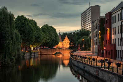 Trees reflecting on canal in city at dusk