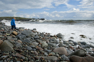 Man standing on rocks at beach against sky