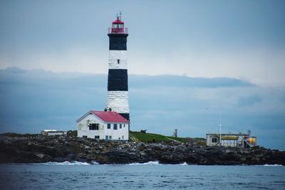 Lighthouse by sea against sky