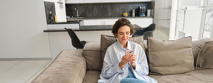 Young woman using mobile phone while sitting on bed at home