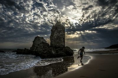 Man walking on shore by sea against sky