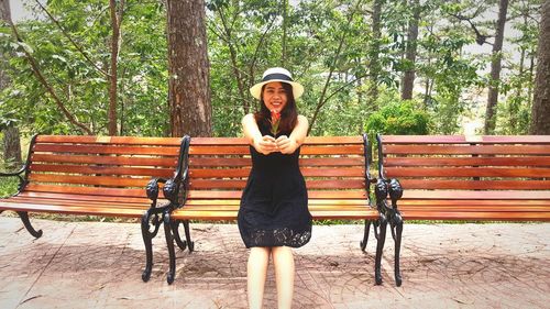 Portrait of young woman giving flowers while sitting on bench at park