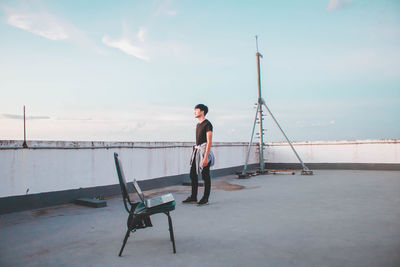 Side view of young man standing on terrace against sky