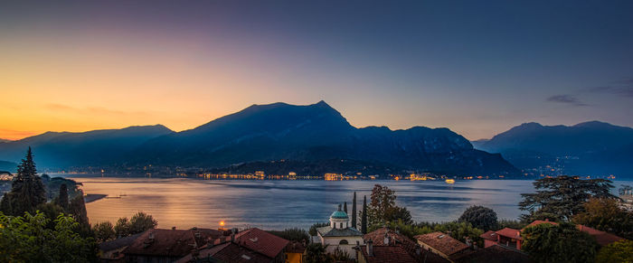 Scenic view of buildings by mountains against sky during sunset