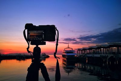 Reflection of person photographing on water against sky during sunset