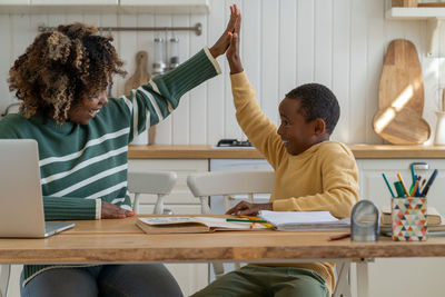 Pleased schoolboy and private tutor giving high five sit at home table celebrating success in study