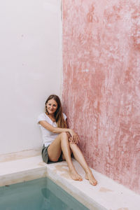 Full length portraits of a blond, caucasian woman leaning against a colored wall in tulum, mexico