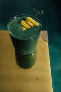 Green spirulina smoothie with pineapple on brass, gold table and teal background