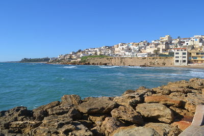 Scenic view of sea by buildings against clear blue sky