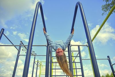 Low angle view of happy girl hanging from a climbing frame in a playground looking at camera.