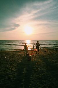 Family enjoying on sea shore against sky during sunset