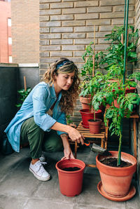 Woman using shovel to fill with soil a pot of plant in urban garden on terrace