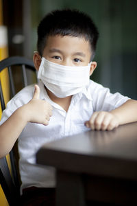 Portrait of boy wearing mask gesturing while sitting at home