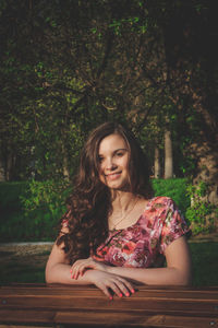 Portrait of smiling young woman sitting against trees