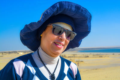 Portrait of smiling young woman standing at beach against clear blue sky