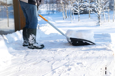 A man in rubber boots with a snow shovel cleans the snow from the terrace of the house