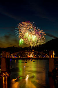 Firework display over river against sky at night