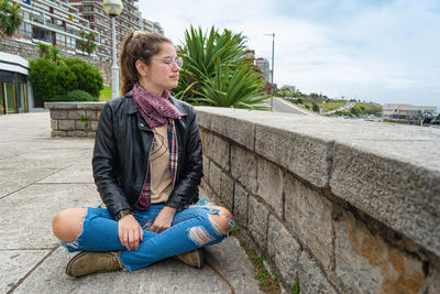 Portrait of young woman sitting on retaining wall