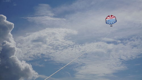 Low angle view of two people parasailing against cloudy sky