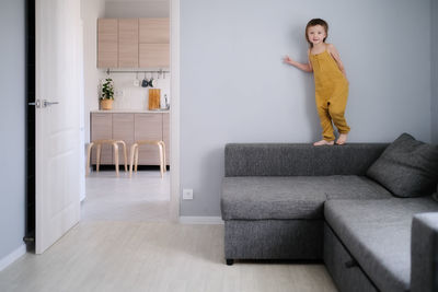 Child jumps and plays on sofa in minimalist living room, gray sofa.