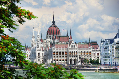 Hungarian parliament building by danube river against sky in city