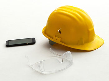 Close-up of hardhat with eyeglasses and mobile on white background