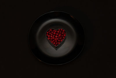 Lingonberries are laid out in the shape of a heart on a black plate on a black background. raw food.