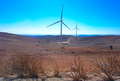 Wind turbines on desert land against blue sky