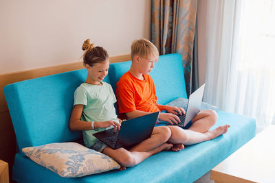 Kids using laptop while sitting on sofa at home